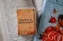 Bourbon & Butterscotch wax melts package on top of an open book with a colorful cover.