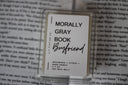 A wax melt pack with the label 'Morally Gray Book Boyfriend' placed on an open book background