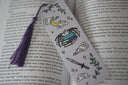 A set of decorative bookmarks with a fantasy theme, including characters and magical elements, placed inside an open book.