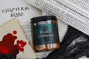 Candle jar labeled 'Blake Drakharrow' on a book background