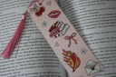 A pink bookmark with a fantasy theme and fun illustrations like lips, books, bow, and chilis