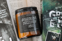 A jar candle with a dark label reading 'IN MY DARK ROMANCE ERA' placed on a surface with an open book in the background.