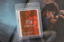 Scented wax melt packaging with 'Kat Fire Fae' design on a blurred background of a couple embracing.