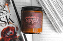 Midwinter in Nyaxia book candle from The Crowns of Nyaxia series surrounded by open books and red poppy