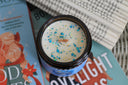 Santa Baby, Slip a Dragon Under the Tree candle top view with blue and gold sprinkles and wooden wick on holiday books