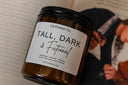 close-up view of a candle labeled 'tall dark and fictional'  in an amber jar displayed on a book