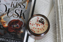 The Kiss of Dusk Shadowborn Duet candle with confetti splatter wax and open fantasy book